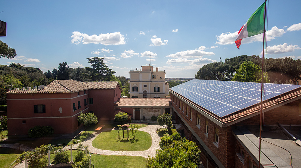 Aerial view of Loyola University Chicago’s Rome Center campus with brick buildings, a courtyard garden, solar panels on the roof, and the Italian flag