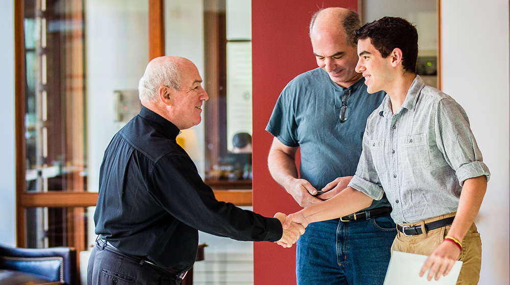 Two men shaking hands with one man standing behind them
