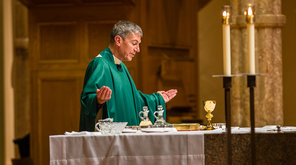 A priest standing at an altar with his arms outstretched 