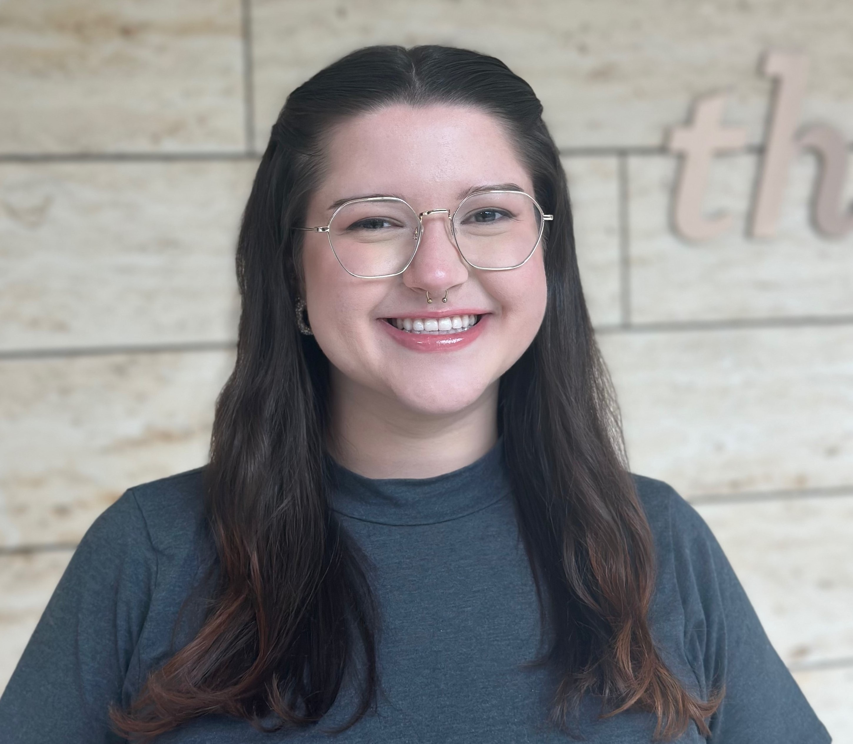 Professional headshot of a smiling woman with glasses against a neutral background