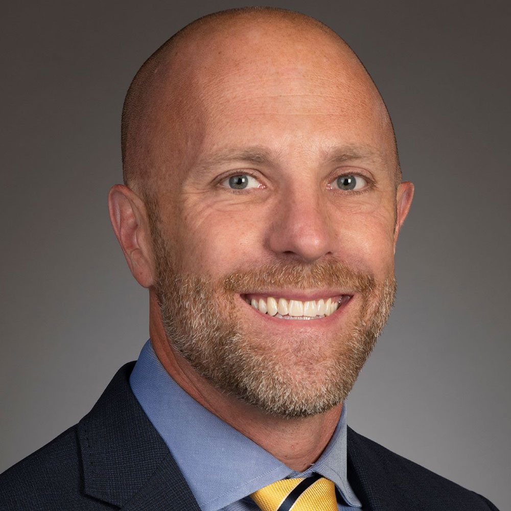 Portrait of a bald man with a trimmed beard smiling, wearing a suit jacket, dress shirt, and yellow tie against a neutral background. Portrait of a bald man with a trimmed beard smiling, wearing a suit jacket, dress shirt, and yellow tie against a neutral background.