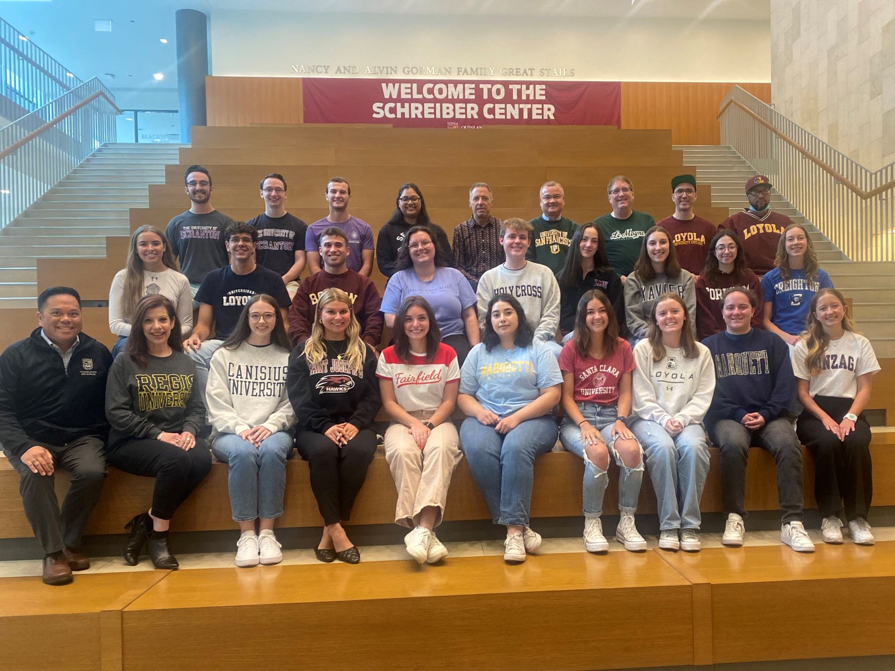 Group of students and staff seated on stairs beneath a “Welcome to the Schreiber Center” banner.