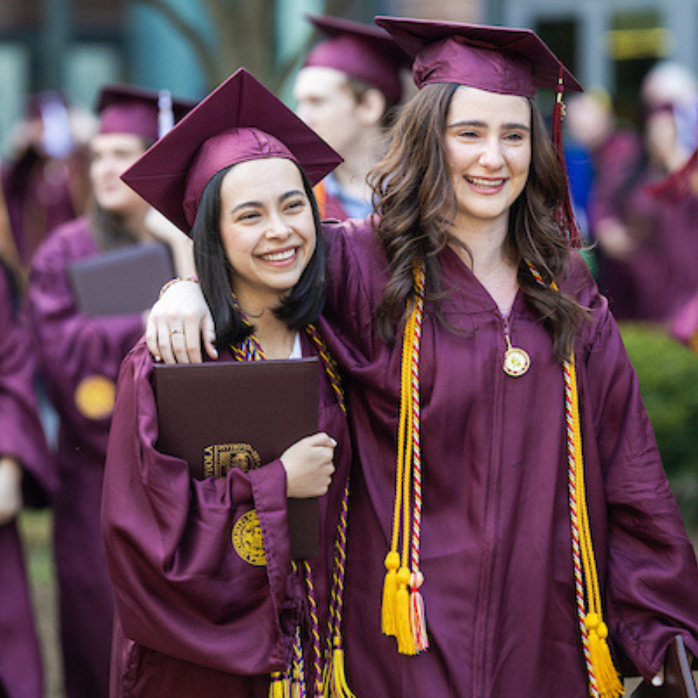 Two Loyola University Chicago graduates celebrating outside with their peers