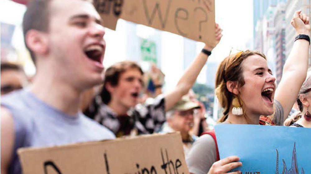 People gathered at a public demonstration holding handmade signs and raising their arms while participating in an outdoor advocacy march in the city.