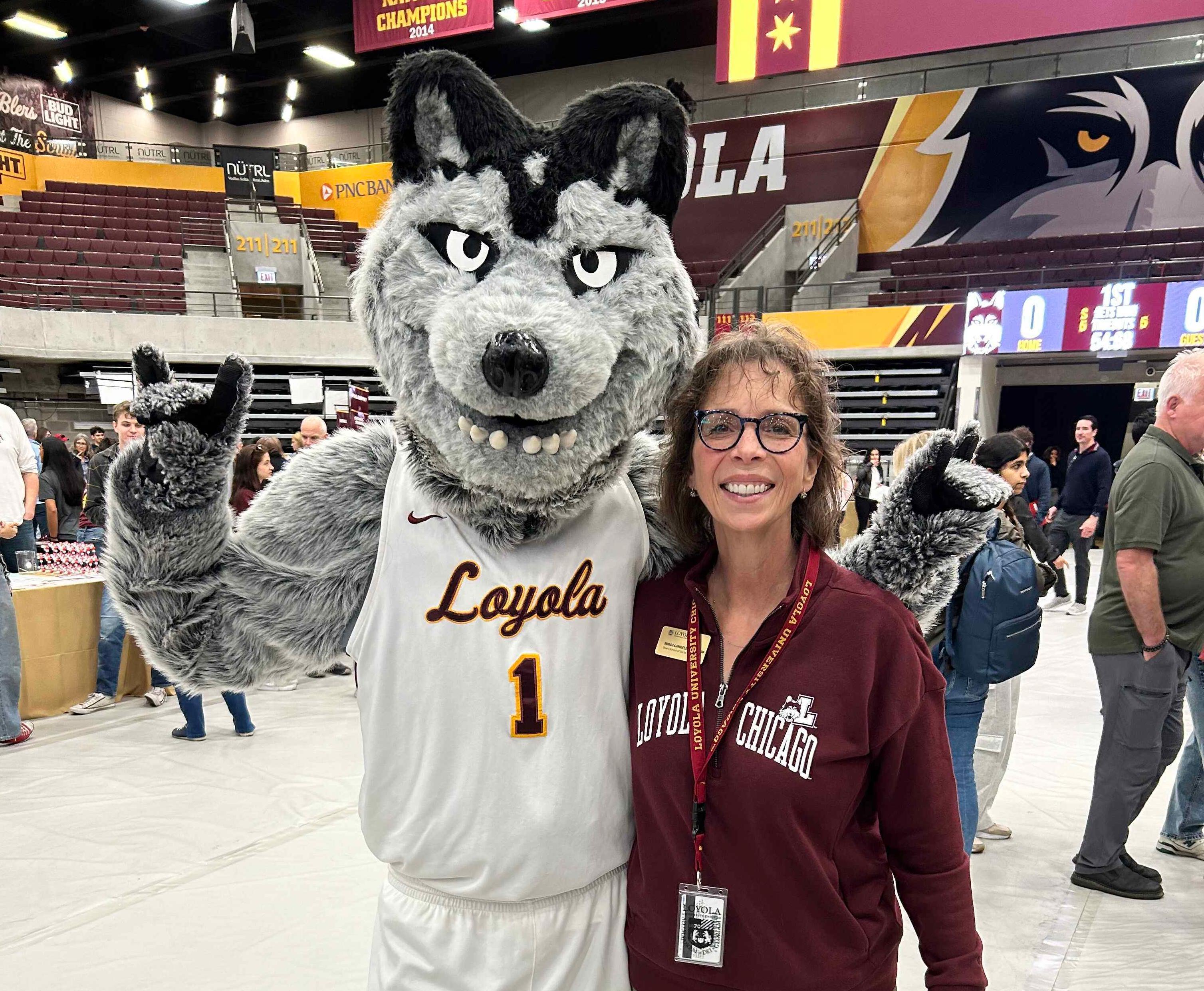 Patricia Findley, DrPH, MSW, LCSW, Dean of the School of Social Work, stands smiling beside the Loyola mascot inside a campus arena.