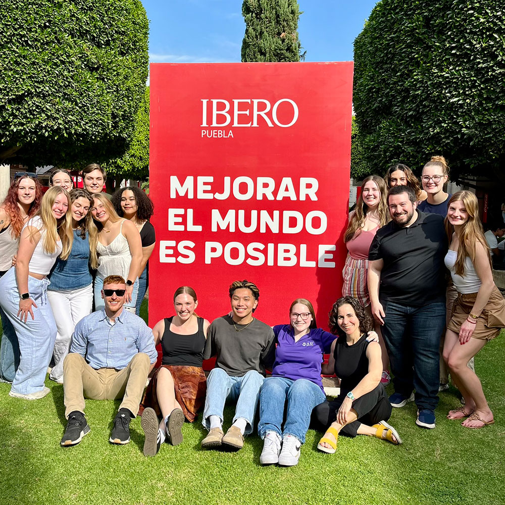 A faculty-leg group of student pose around a sign that reads MEJORAR EL MUNDO ES POSIBLE. It is possible to make the world better.