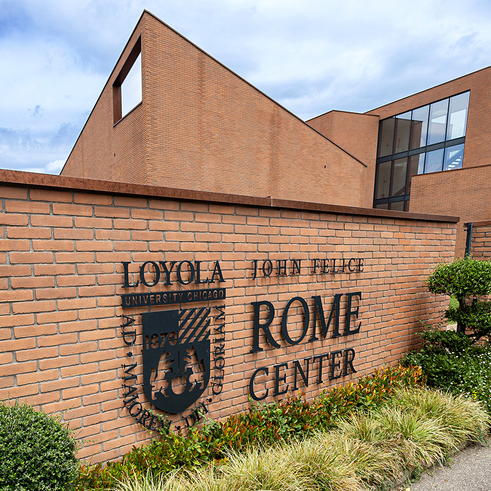 John Felice Rome Center Entrance under an expansive sky. A dark metal Loyola University Chicago logo is fixed on the wall near the entrance.