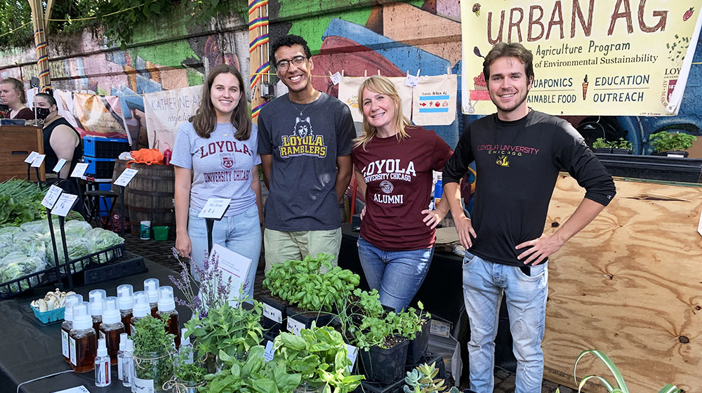 Students and staff at an urban agriculture booth displaying plants and products.