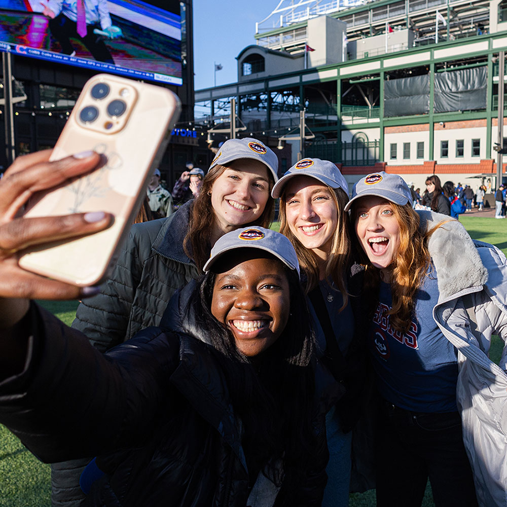 A group of Loyola University Chicago students take a lively selfie at Wrigley Field during a Chicago Cubs event.