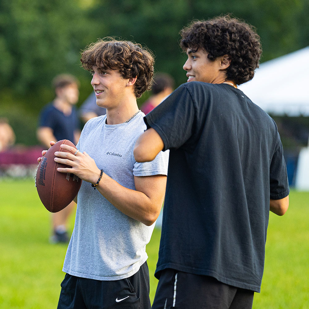 Two undergraduate students talk while throwing a football on the Lake Shore Campus