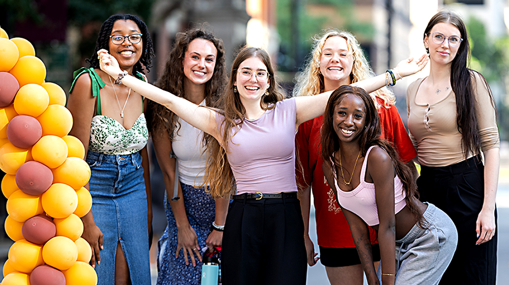 A diverse group of young women at the Loyola Block Party pose near a 12-foot-tall grouping of balloons that spell LOYOLA.