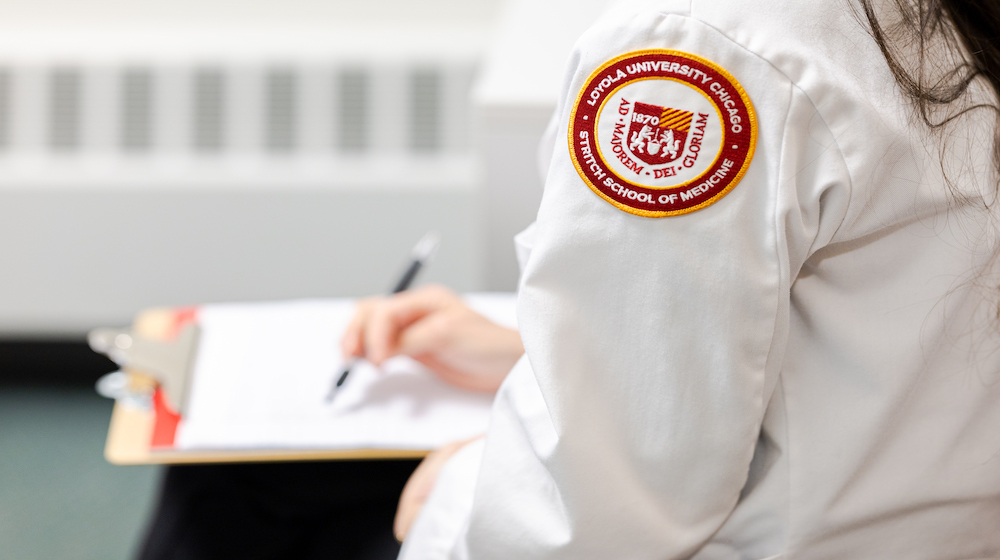 Loyola University Chicago Stritch School of Medicine patch on a white coat as a student completes paperwork