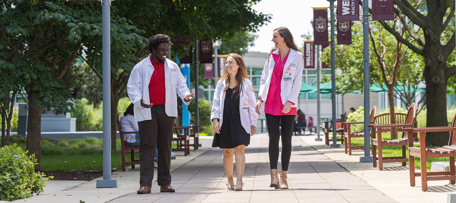 three students smiling in white coats outside