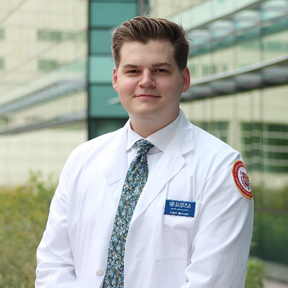 Portrait of a smiling man in a white lab coat standing outside a modern building