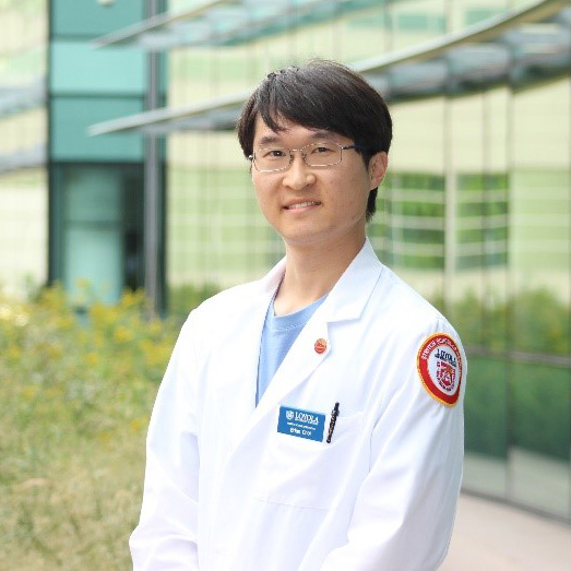 Portrait of a man in a white lab coat standing outdoors in front of a modern building