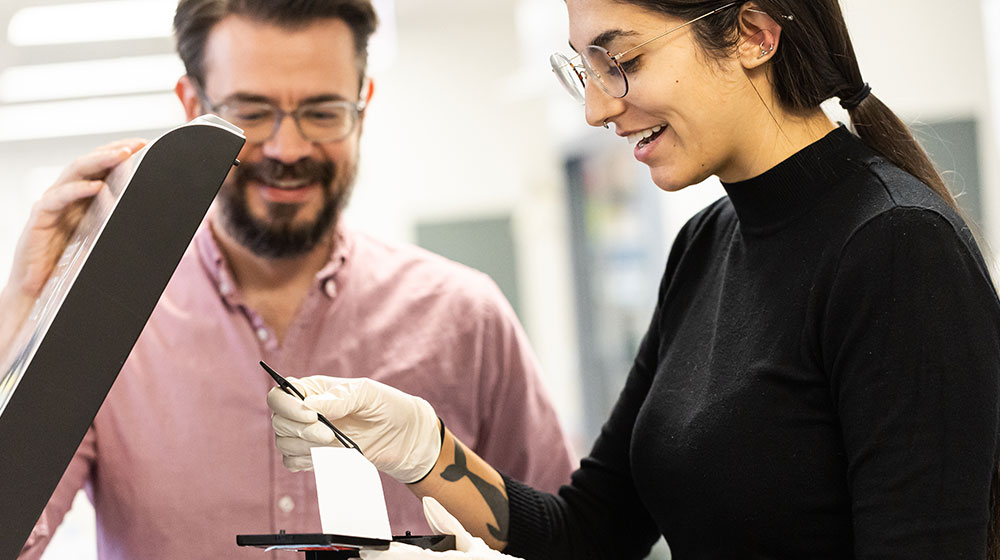 Student using lab equipment with a tool while an instructor observes nearby.