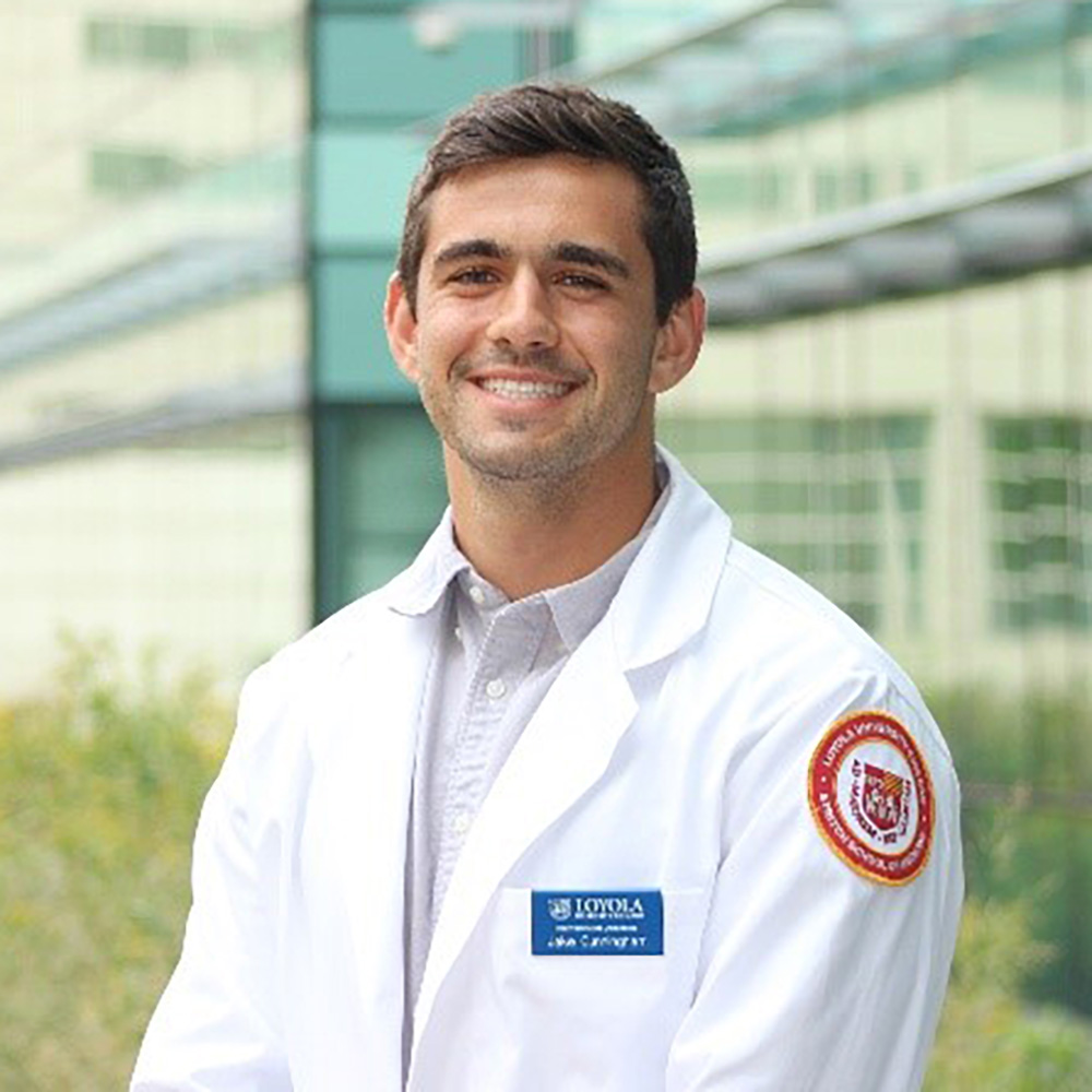 Portrait of a smiling man in a white lab coat standing outside a modern building