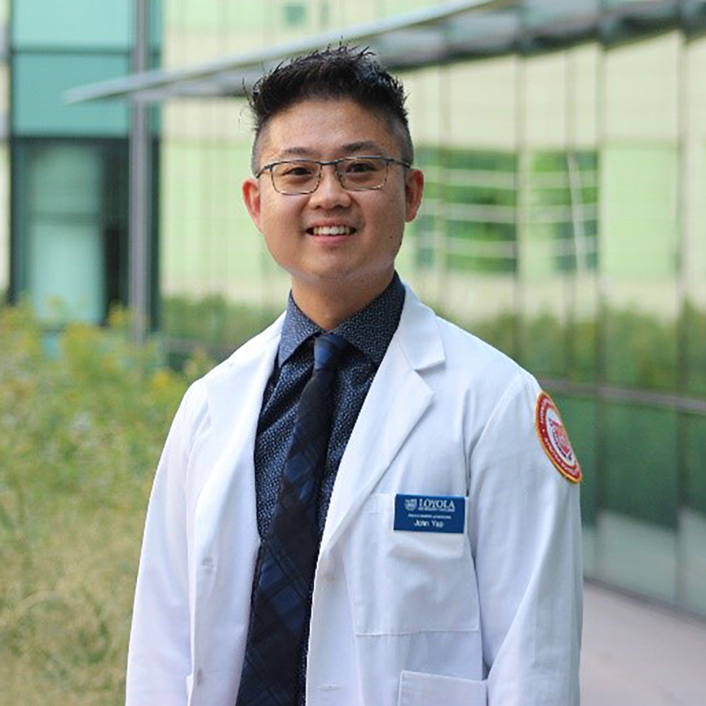 Portrait of a smiling man in a white lab coat standing outside a modern glass building