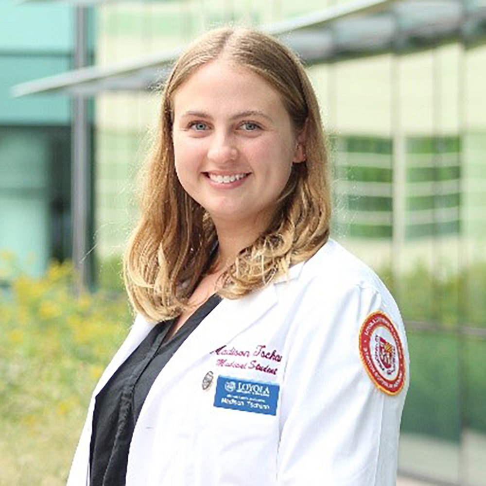 Portrait of a smiling woman in a white lab coat standing outside a modern building