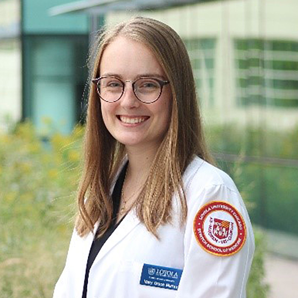 Portrait of a smiling woman in a white lab coat standing outside a modern building