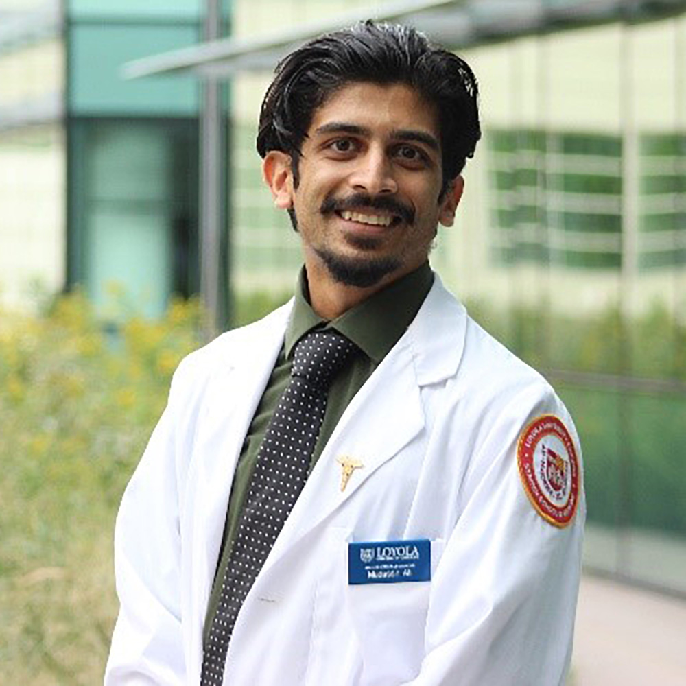 Portrait of a smiling man in a white lab coat standing outside a modern building