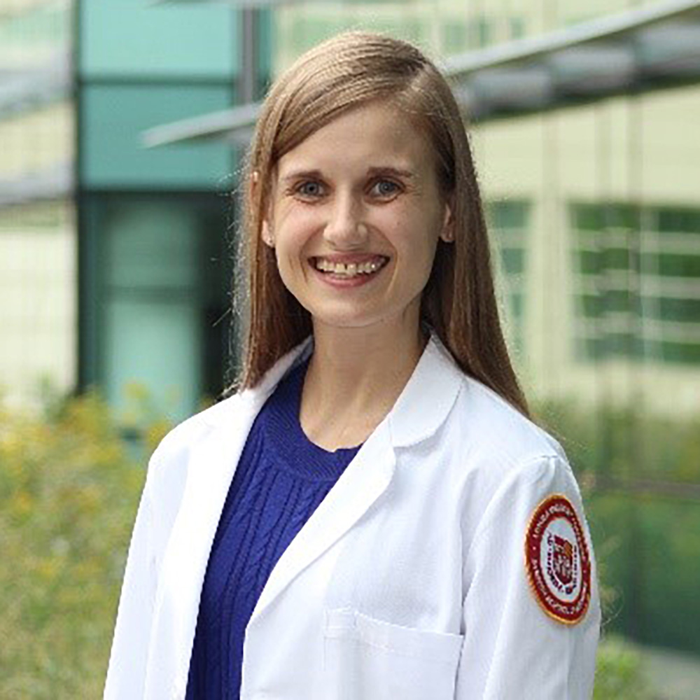 Portrait of a smiling woman in a white lab coat standing outdoors in front of a modern building