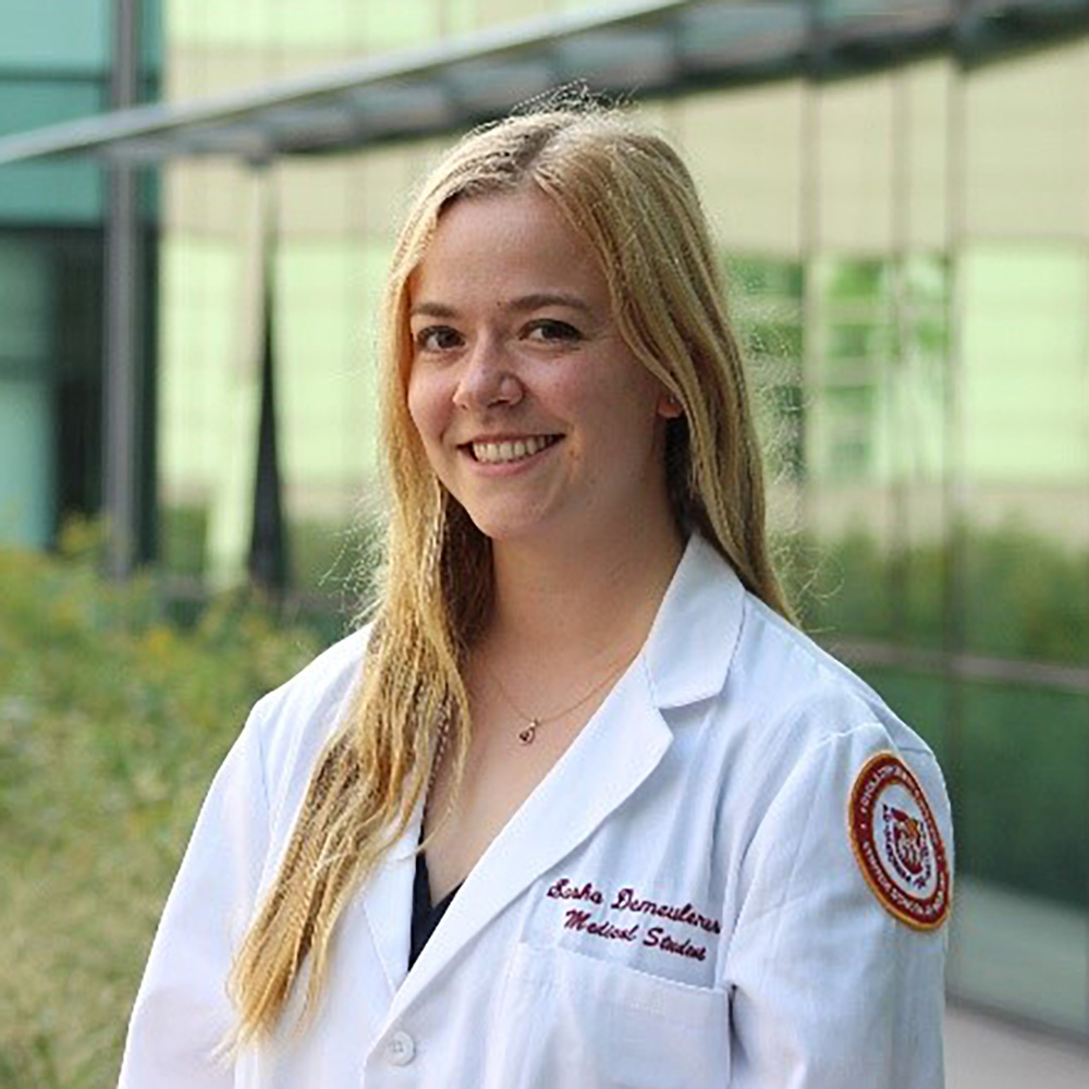 Portrait of a smiling woman in a white lab coat standing outside a modern building