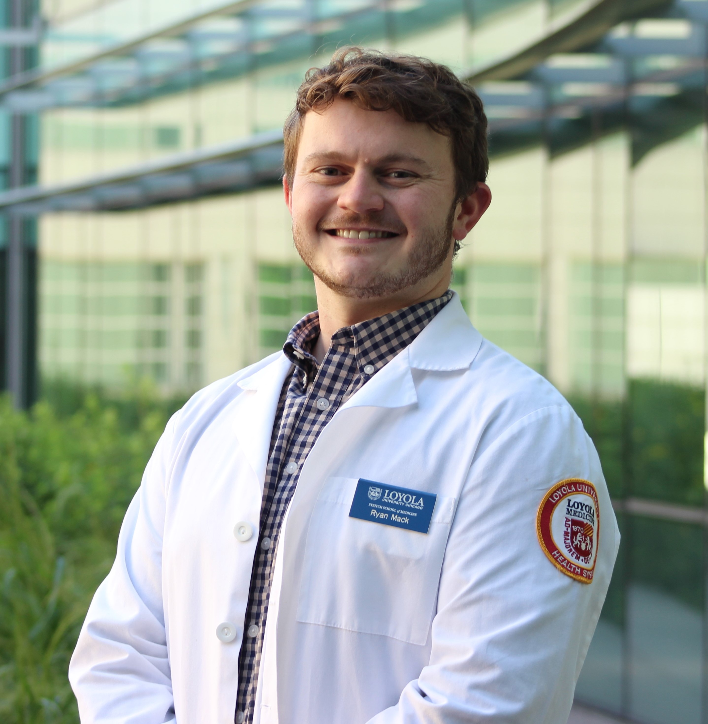 Portrait of a smiling man in a white lab coat standing outside a glass building