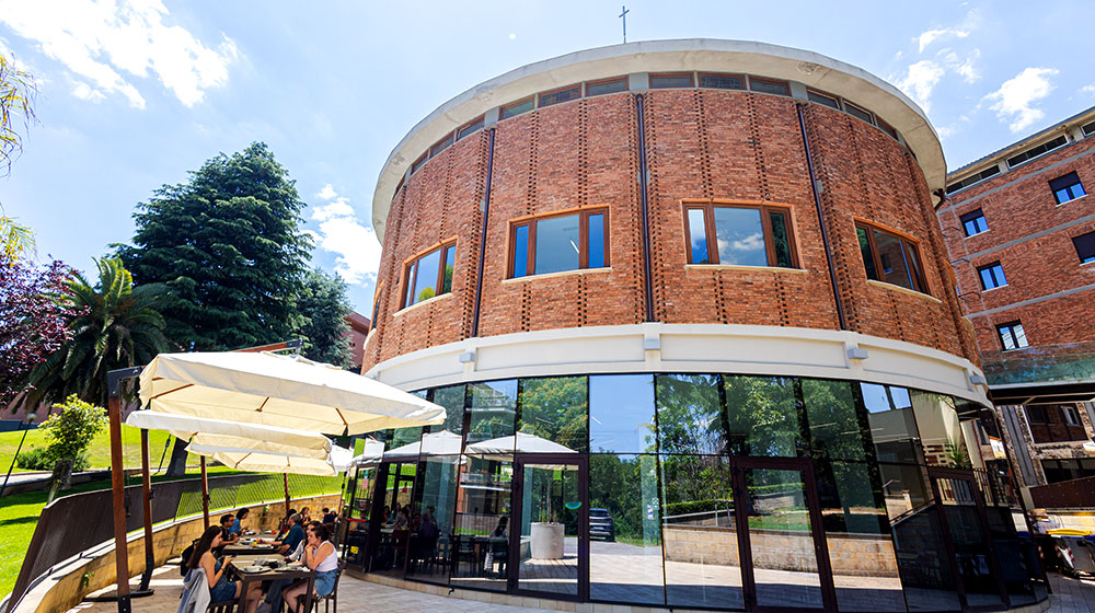 Exterior view of Loyola University Chicago’s Rome Center, a round brick building with glass entrance and outdoor seating.