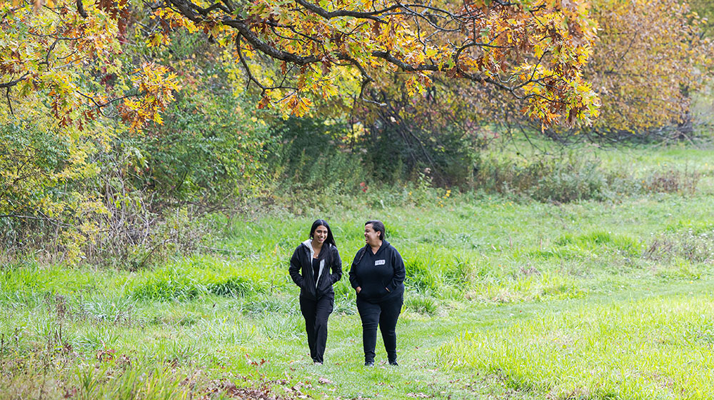 Two Loyola University Chicago students walking on grassy path at Retreat and Ecology Campus in Woodstock, IL.